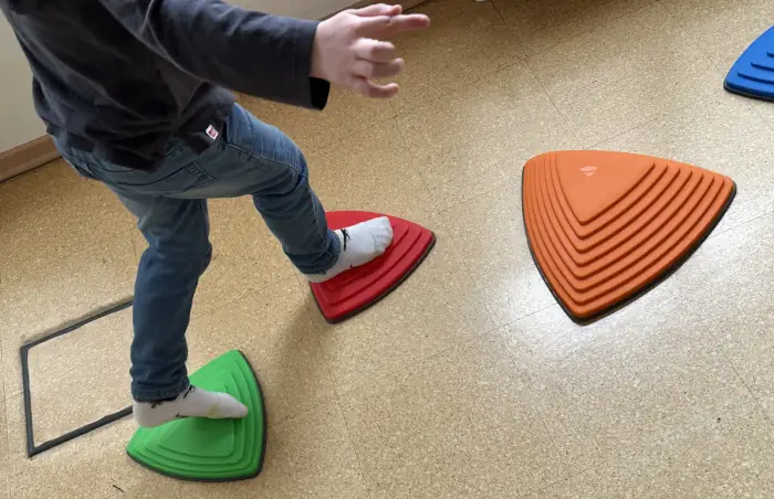 Bewegungstherapie: Ein Kind läuft über farbige Trittmarker.