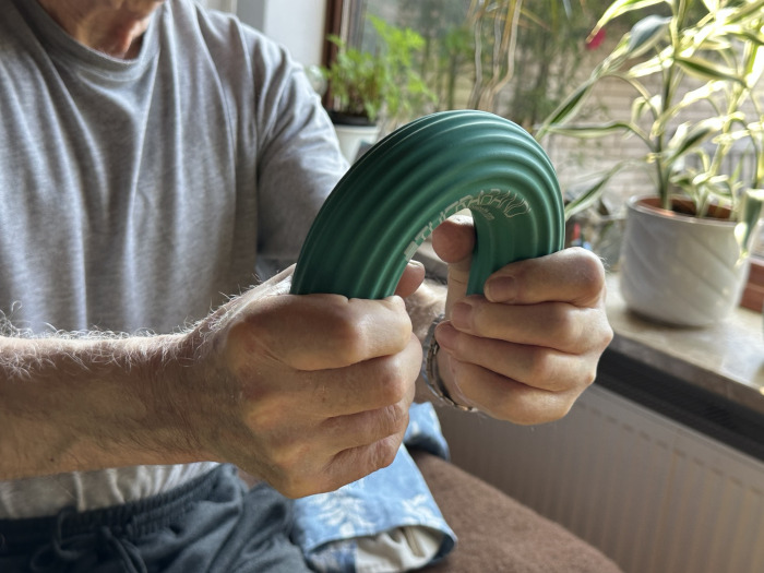 Geriatrie: Eine ältere Person biegt mit beiden Händen die Enden eines dicken Gummistabs zusammen.